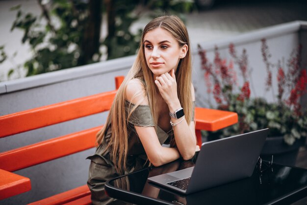 Mujer de negocios joven que trabaja en la computadora portátil afuera en un café