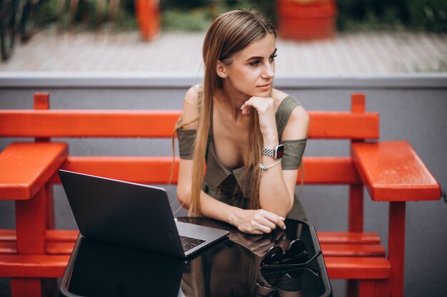 Mujer de negocios joven que trabaja en la computadora portátil afuera en un café