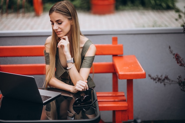 Mujer de negocios joven que trabaja en la computadora portátil afuera en un café