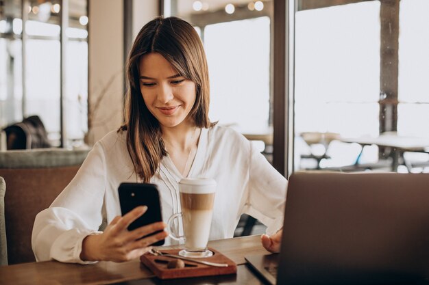 Mujer de negocios joven que trabaja en línea en un café y tomando café