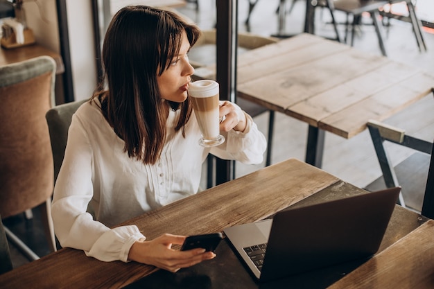 Mujer de negocios joven que trabaja en línea en un café y tomando café