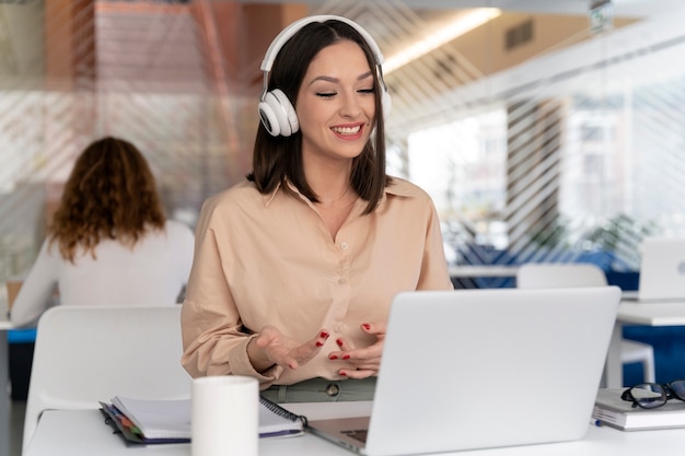 Mujer de negocios joven que trabaja en la oficina con ordenador portátil y auriculares