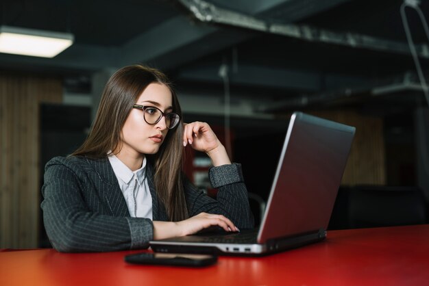 Mujer de negocios joven que usa el ordenador portátil en la tabla