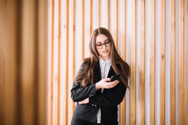 Mujer de negocios joven que usa smartphone en la pared