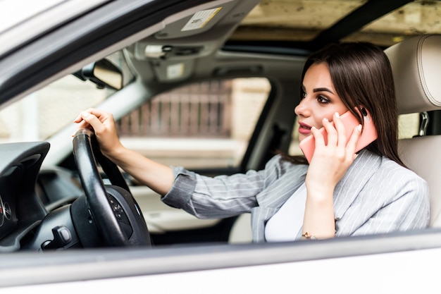 Mujer de negocios joven que usa su teléfono mientras conduce el coche