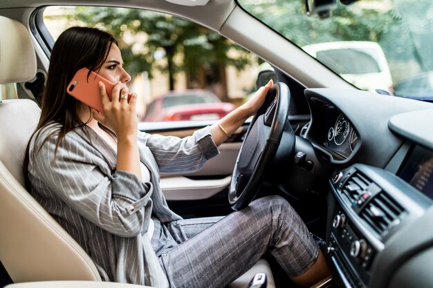Mujer de negocios joven que usa su teléfono mientras conduce el coche