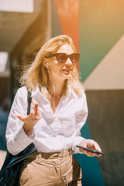 Mujer de negocios joven rubia en música que escucha de la luz del sol en gesticular del teléfono móvil