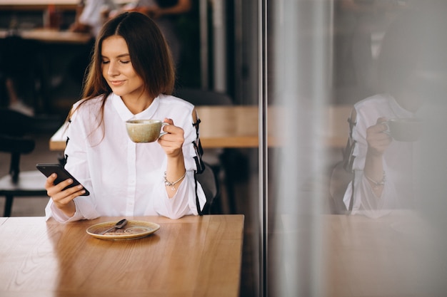 Mujer de negocios joven sentado en un café con café y teléfono