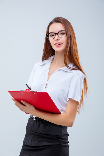 La mujer de negocios joven sonriente con lápiz y tableta para notas sobre gris