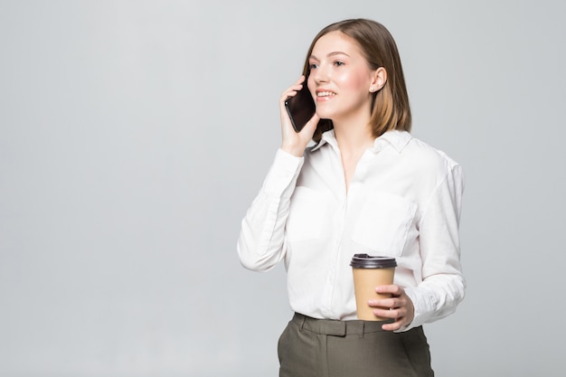 Mujer de negocios joven sosteniendo una taza de café y un teléfono sobre blanco aislado