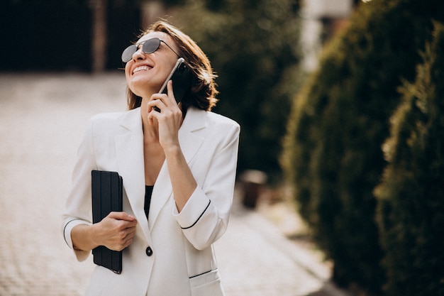 Mujer de negocios joven en traje blanco hablando por teléfono al aire libre