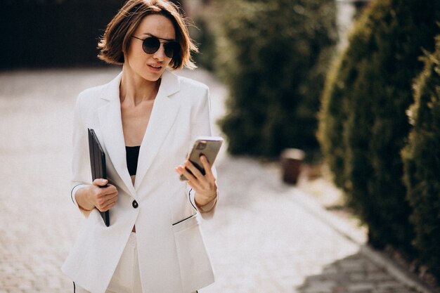 Mujer de negocios joven en traje blanco hablando por teléfono al aire libre