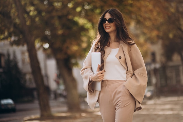 Foto gratuita mujer de negocios joven en traje de negocios con portátil en la calle