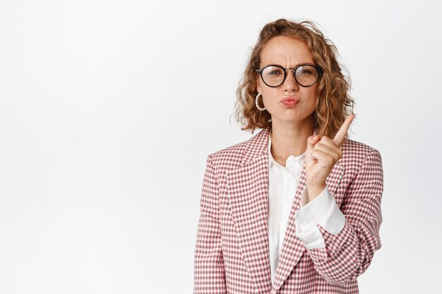 Mujer de negocios mandona con gafas regañando a alguien, agitando el dedo en señal de desaprobación, jefe alrededor, de pie en blanco