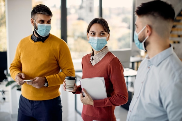 Mujer de negocios con mascarilla mientras habla con colegas masculinos en la oficina