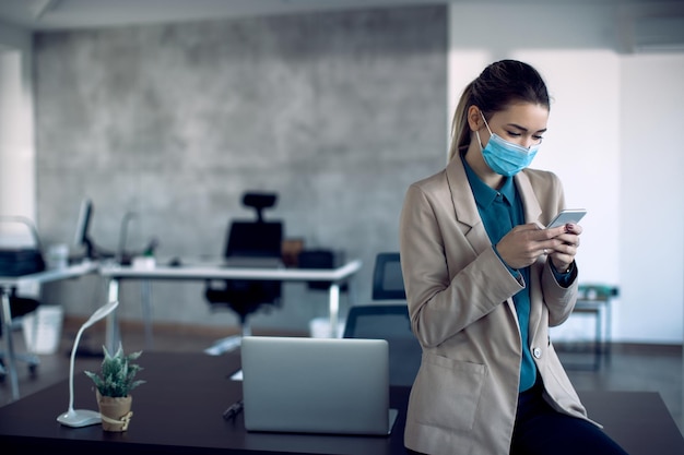 Foto gratuita mujer de negocios con mascarilla protectora enviando mensajes de texto por teléfono móvil en la oficina