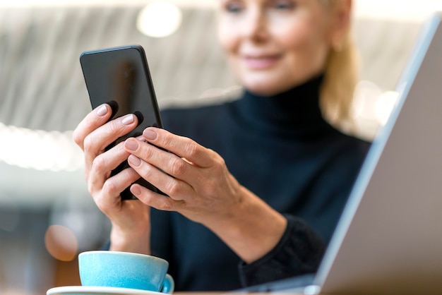 Mujer de negocios mayor Defocused que trabaja en la computadora portátil y el teléfono inteligente