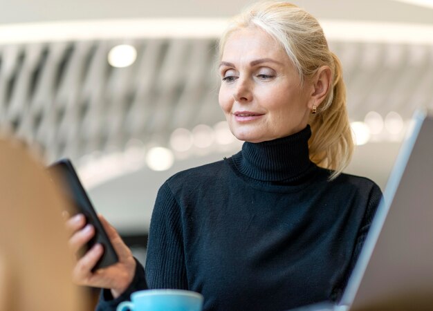 Mujer de negocios mayor que trabaja en la computadora portátil y el teléfono inteligente mientras toma un café