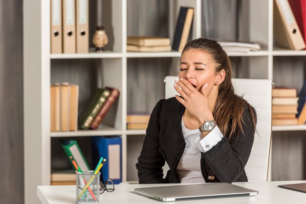 Mujer de negocios morena bostezando en su oficina