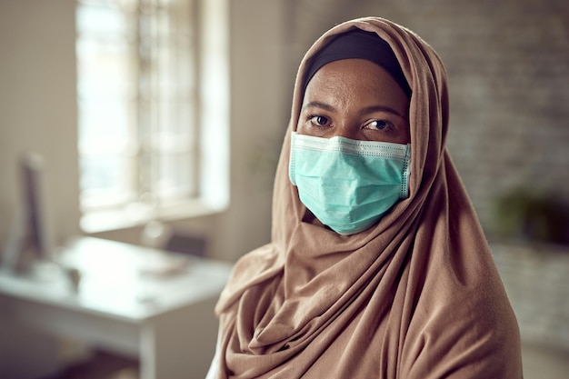 Mujer de negocios musulmana con mascarilla en la oficina durante la epidemia de coronavirus y mirando la cámara