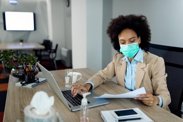 Mujer de negocios negra con mascarilla mientras revisa el papeleo en la oficina