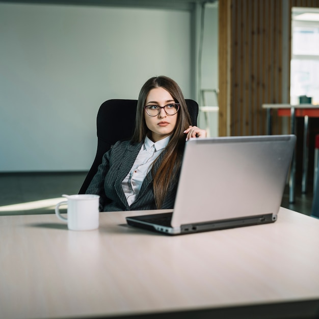 Mujer de negocios pensativa con el ordenador portátil en la tabla