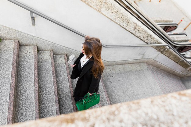 Mujer de negocios con periódico y bolsa subiendo escaleras