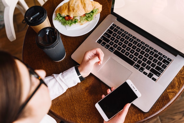 Mujer de negocios con portátil y smartphone en cafetería