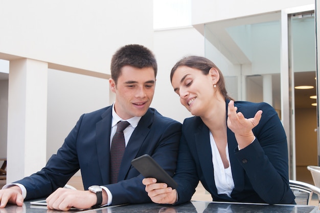 Mujer de negocios positiva que muestra la pantalla del teléfono inteligente al colega