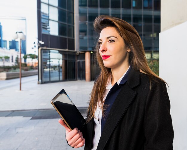 Mujer de negocios que se coloca con la tableta afuera