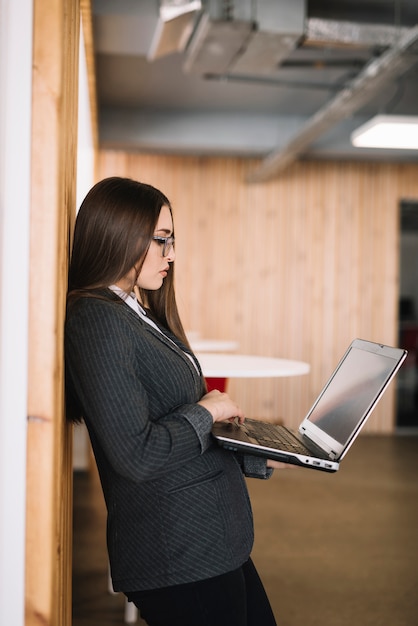 Mujer de negocios que mecanografía en el teclado del ordenador portátil en la pared