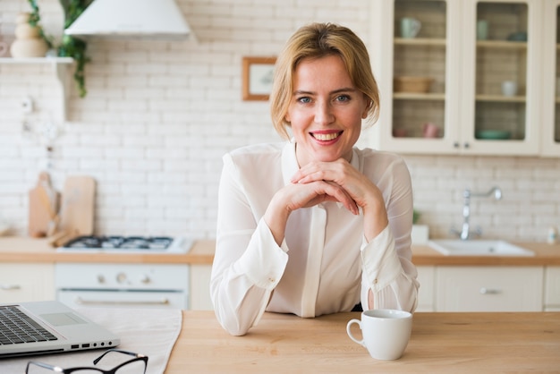 Mujer de negocios que se sienta con la taza de café y el ordenador portátil