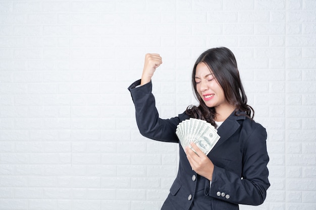 La mujer de negocios que sostenía el billete de banco, cobraba por separado, pared de ladrillo blanca Hizo gestos con lenguaje de signos.