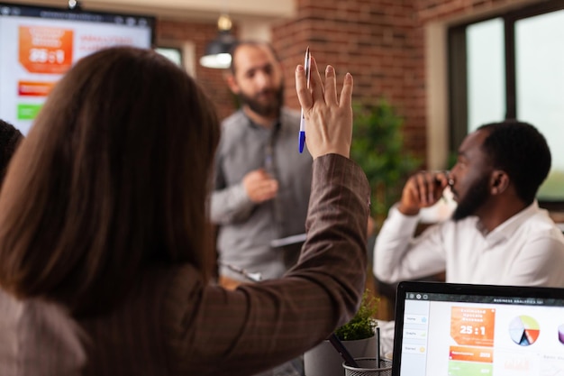 Mujer de negocios que tiene una mano ascendente con una pregunta de marketing durante una reunión de negocios trabajando en la presentación de la empresa en la oficina de inicio. Diversos empresarios discutiendo estrategia analizando gráficos