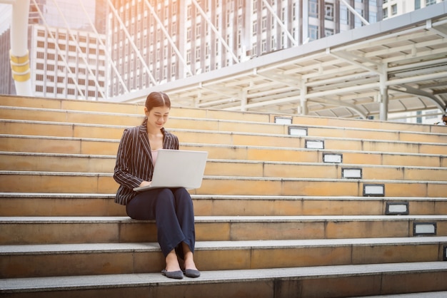 La mujer de negocios que usa la computadora portátil se sienta en los pasos. Gente de negocios concepto.