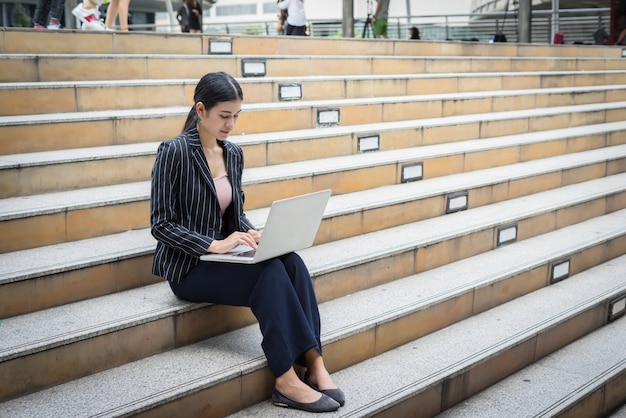 La mujer de negocios que usa la computadora portátil se sienta en los pasos. Gente de negocios concepto.