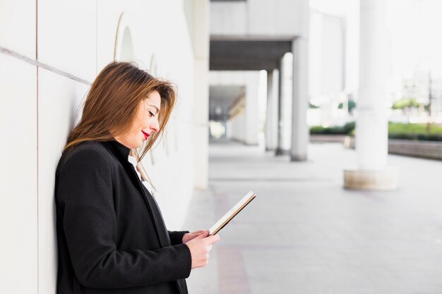 Mujer de negocios que usa la tableta que se inclina en la pared