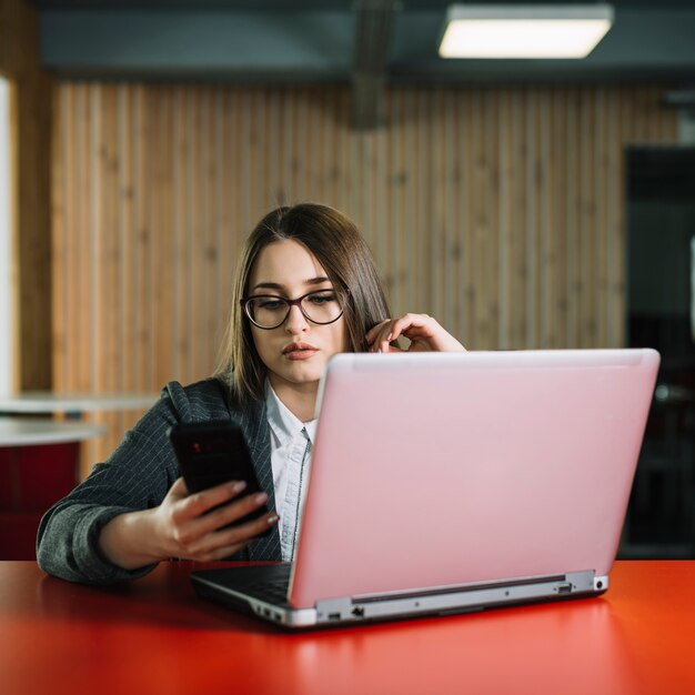 Mujer de negocios que usa teléfono inteligente en la mesa con el ordenador portátil