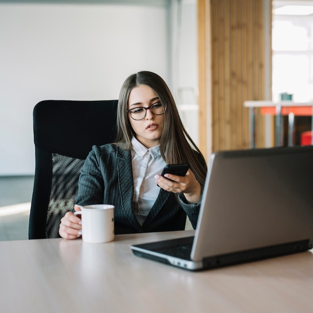 Mujer de negocios que usa teléfono inteligente en la mesa