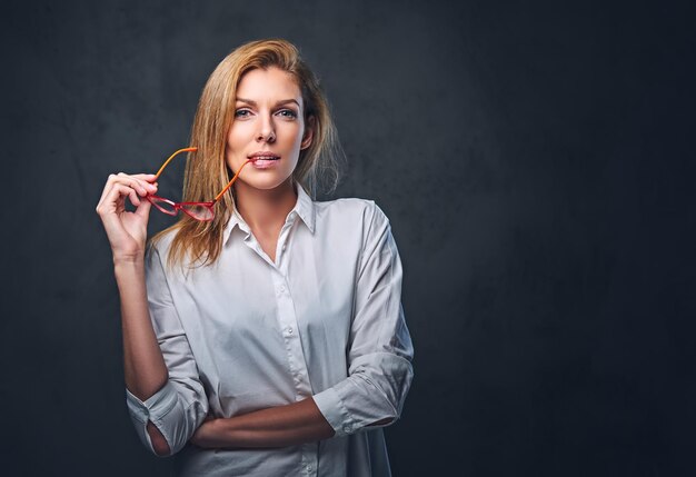 Mujer de negocios rubia atractiva en una camisa blanca sobre fondo gris.