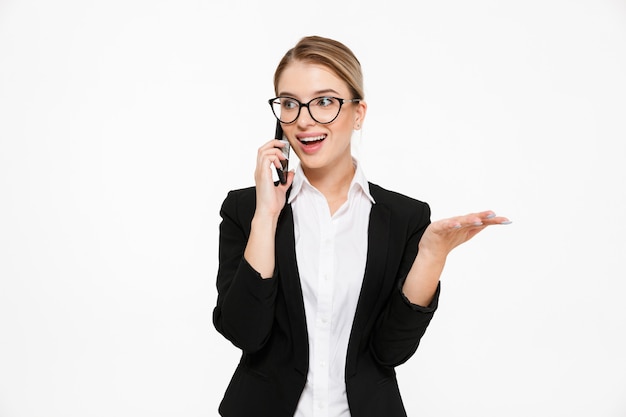 Mujer de negocios rubia feliz sorprendida en anteojos hablando por teléfono y mirando a otro lado sobre blanco