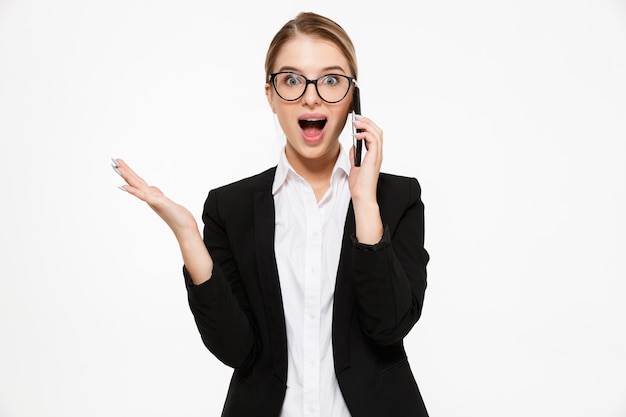 Mujer de negocios rubia feliz sorprendida en anteojos hablando por teléfono