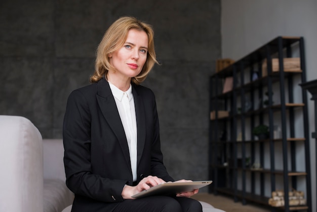 Mujer de negocios rubia pensativa que se sienta con la tableta