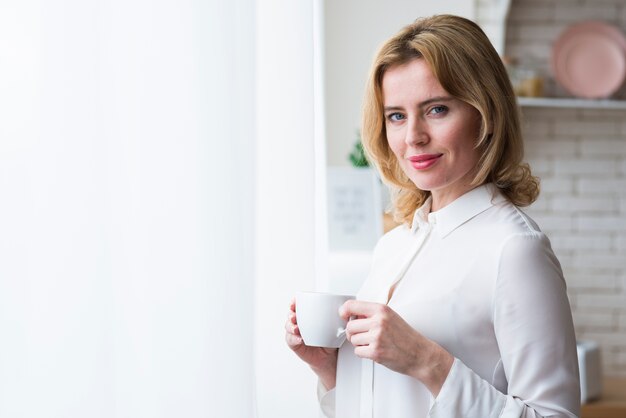 Mujer de negocios rubia que se coloca con la taza de café