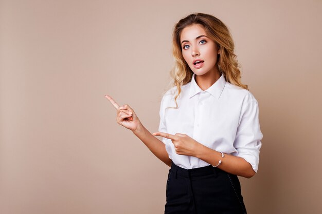 Mujer de negocios rubia que destaca y que mira en la pared beige. Vistiendo ropa de trabajo elegante. Copiar espacio para texto.