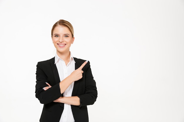 Mujer de negocios rubia sonriente que señala lejos sobre blanco