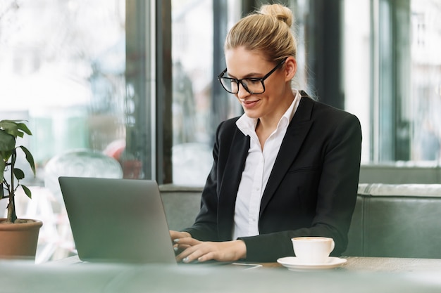 Mujer de negocios rubia sonriente que usa la computadora portátil.