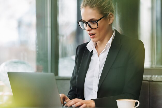 Mujer de negocios rubia sorprendida usando laptop