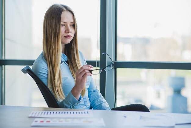 Mujer de negocios rubia sujetando gafas