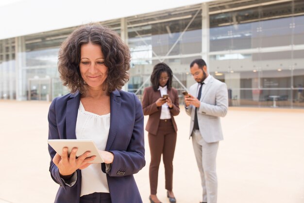 Mujer de negocios satisfecha feliz que usa la tableta afuera